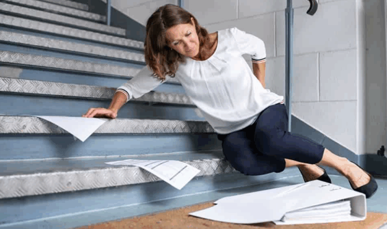 Woman slipping and falling on staircase, holding her back in pain, with papers scattered around.